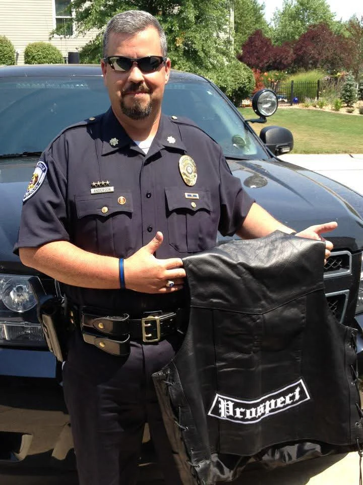 A uniformed police officer holding a black leather vest with an embroidered Prospect patch, made by Independence Embroidery in Owensville, Missouri.