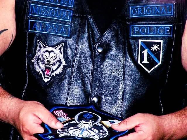 A motorcycle club member holding an embroidered center patch against a black leather vest with embroidered front tabs, made by Independence Embroidery in Owensville, Missouri.