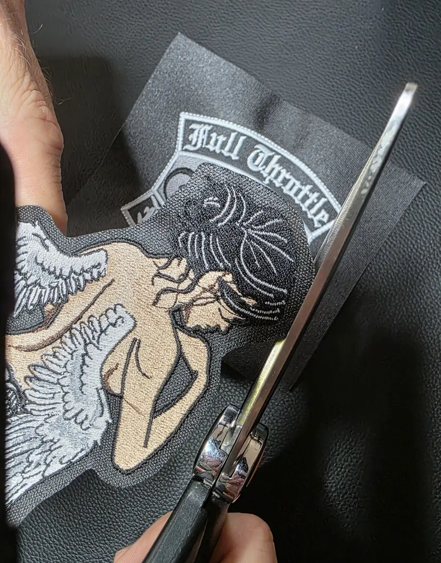 A hand cutting the border of an embroidered patch with scissors at Independence Embroidery in Owensville, Missouri.