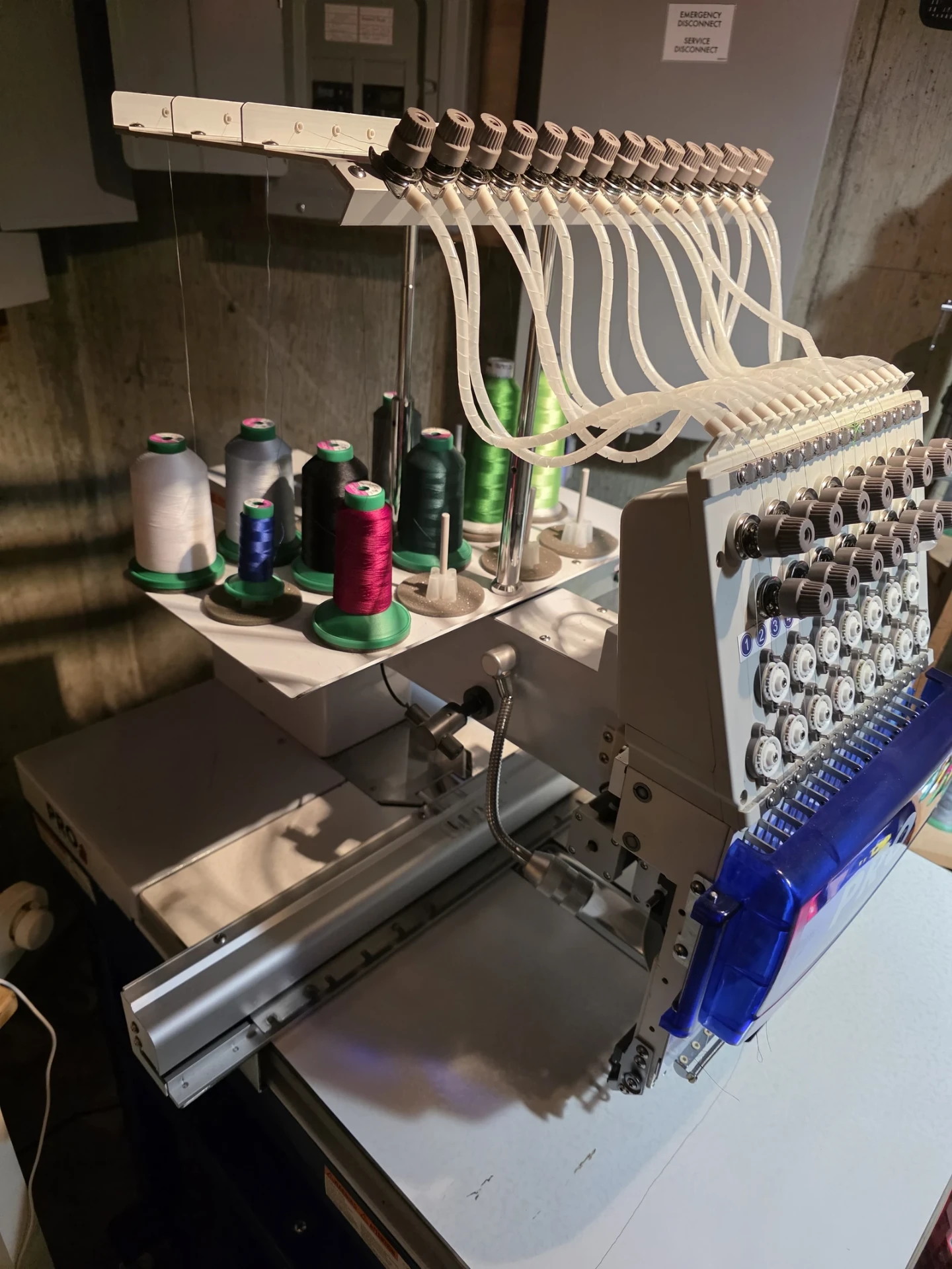 The head of a commercial embroidery machine with sixteen threaded needles and cones of thread, at Independence Embroidery in Owensville, Missouri.