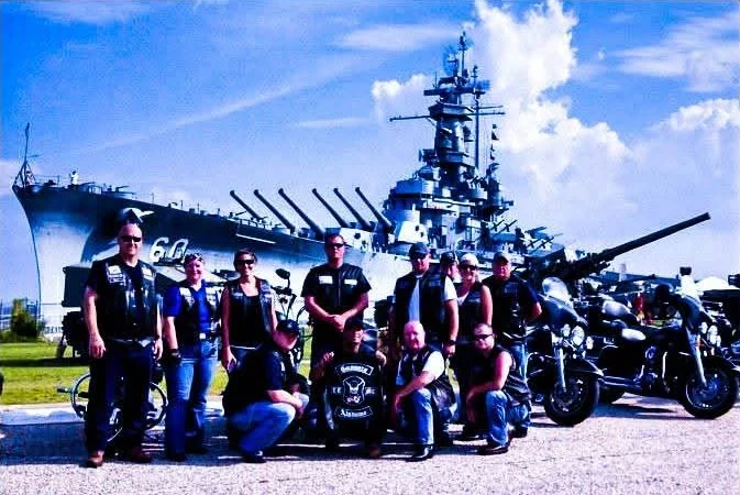 Motorcycle club members in embroidered colors standing in front of a battleship memorial, patches by Independence Embroidery.