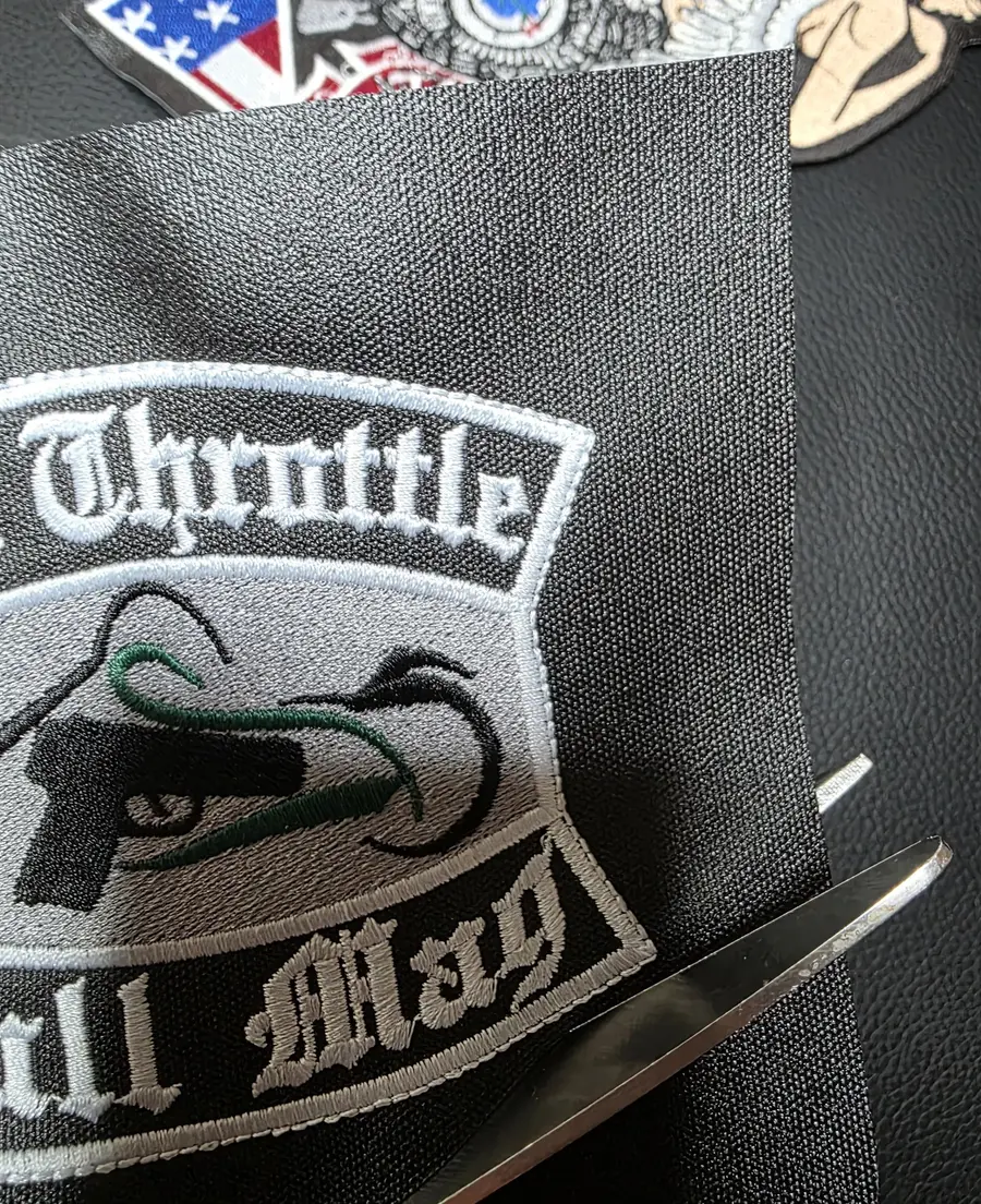 A finished embroidered patch on a sheet of grey coated twill with scissors alongside, before the border is cut.