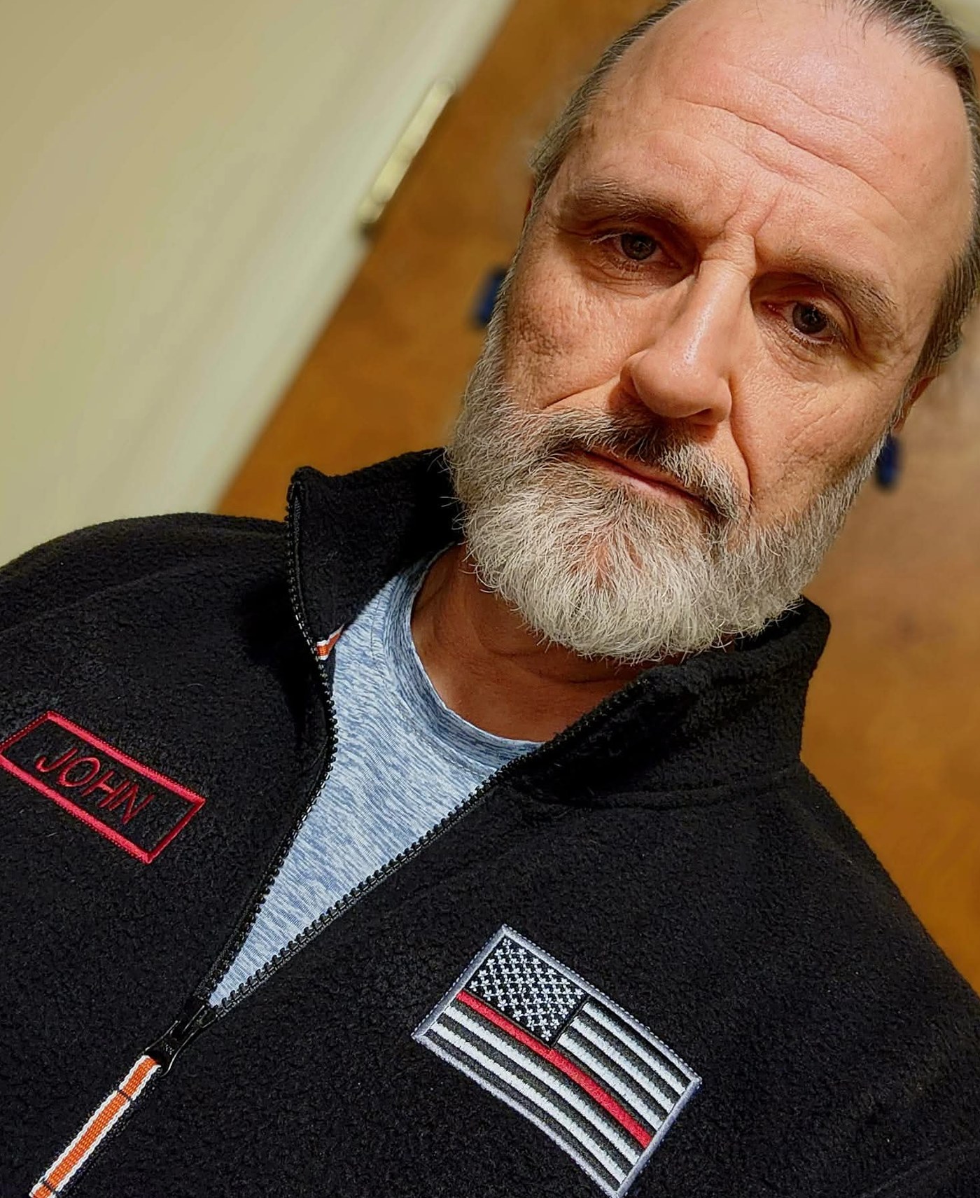 The owner of Independence Embroidery wearing an embroidered name patch and a thin red line flag patch on a black jacket.