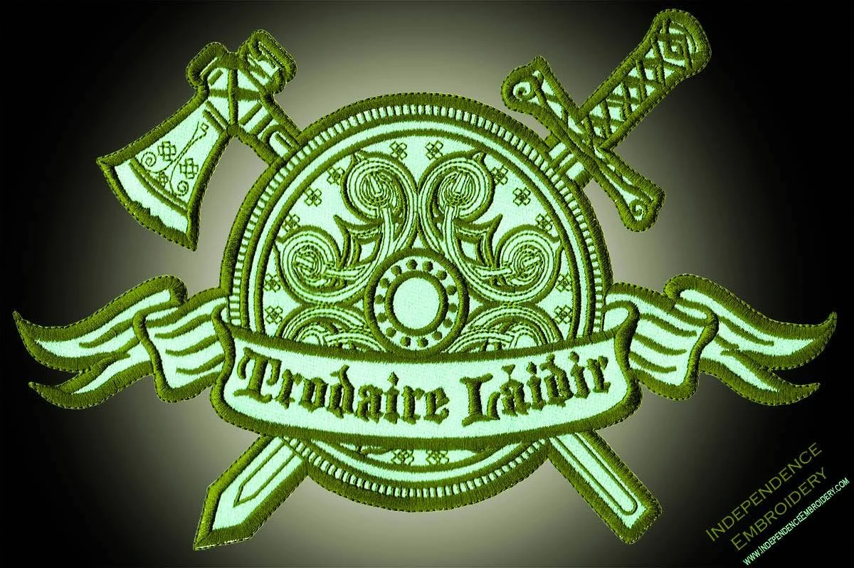 An embroidered shield patch with a crossed axe and sword and a lettered banner, made by Independence Embroidery in Owensville, Missouri.