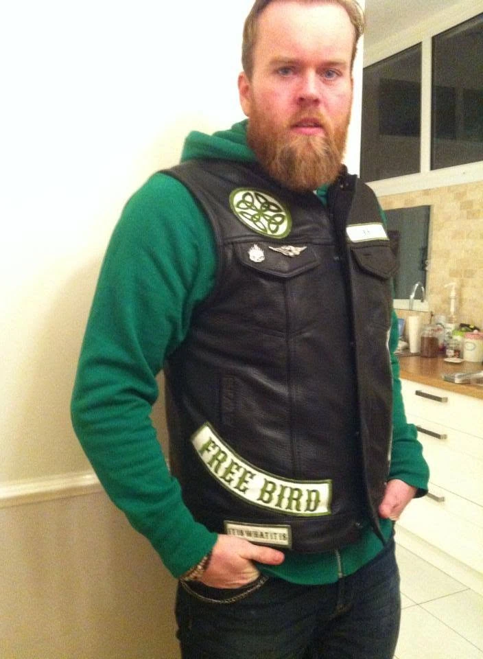 A rider wearing a black leather vest with a green and cream embroidered Celtic knot, name tab, and bottom rocker, made by Independence Embroidery in Owensville, Missouri.
