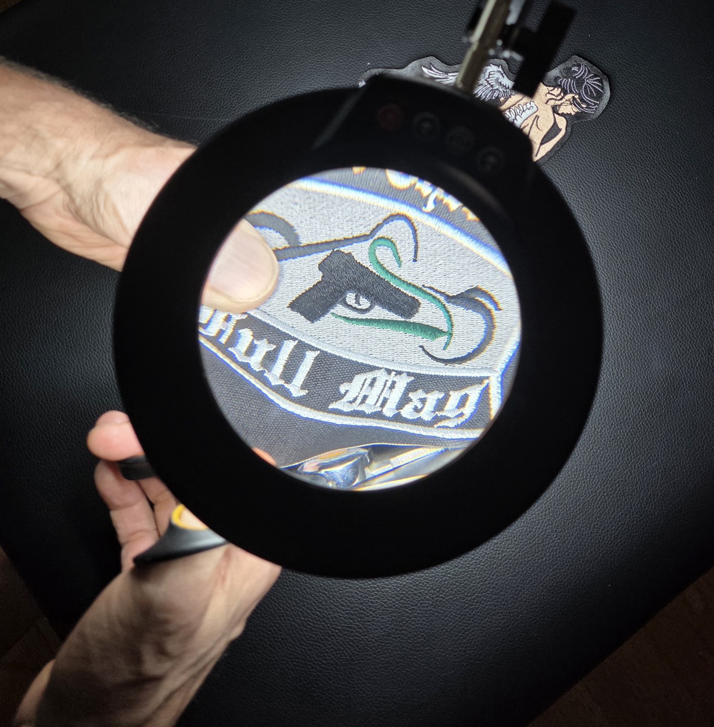 A finished club patch seen enlarged through a hand-held magnifier.
