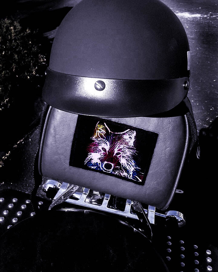 Embroidered wolf patch mounted on the padded seat rest of a motorcycle, helmet resting above it.