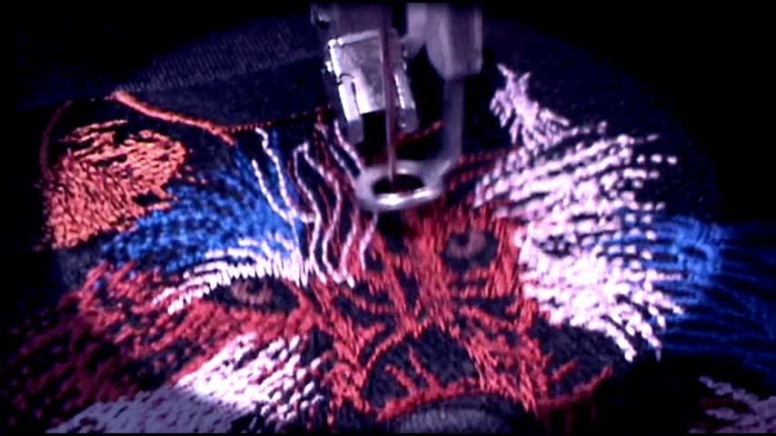 Silent loop of an embroidery machine stitching colored thread into a wolf design on black fabric.